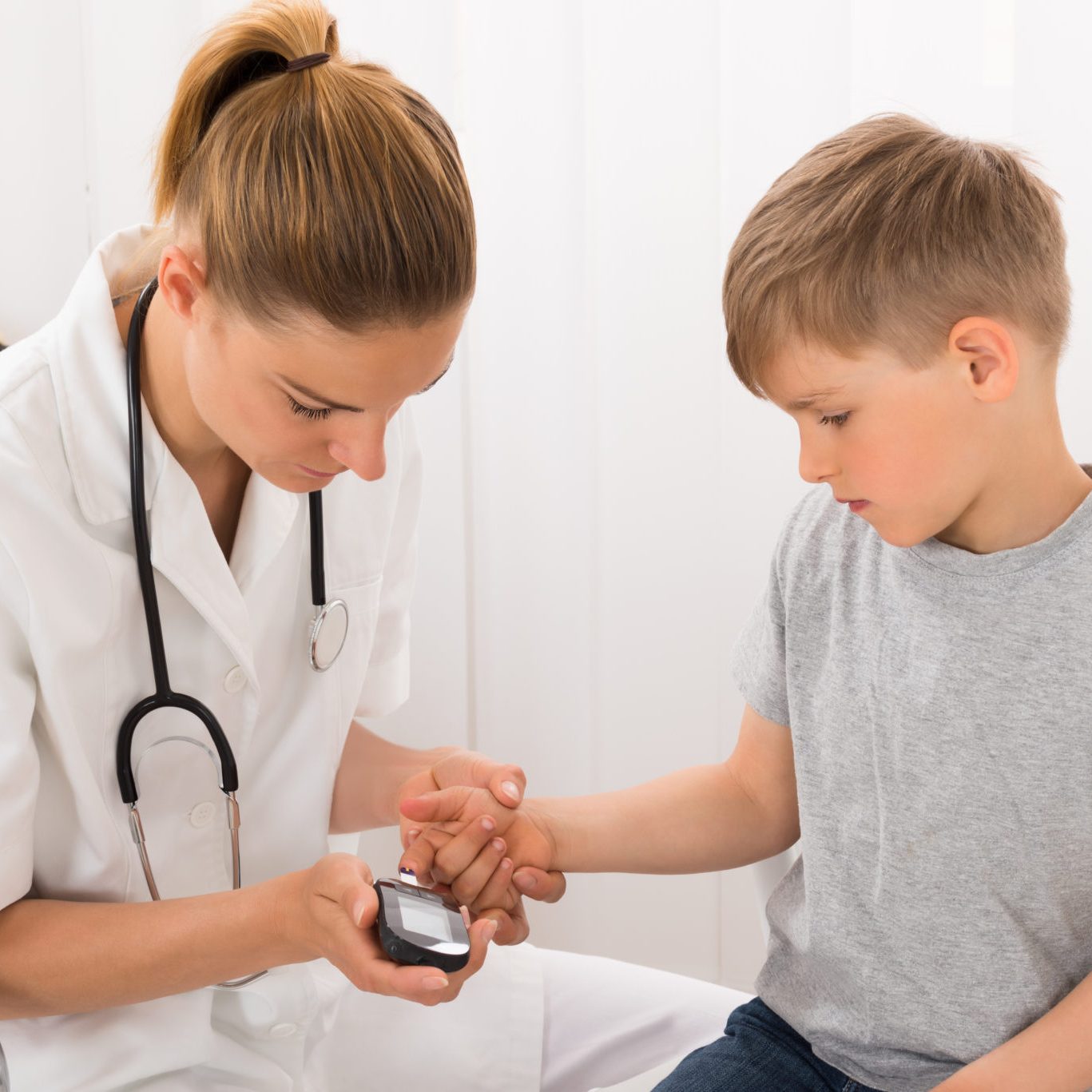 Female Doctor Examining Blood Sugar Of Little Boy With Glucometer